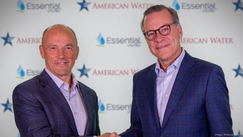 Two executives shaking hands before company backdrop